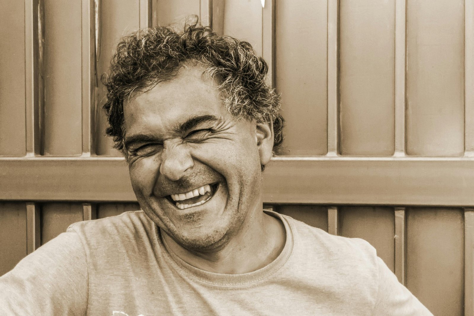 Close-up sepia portrait of a happy, laughing man against a textured background.
